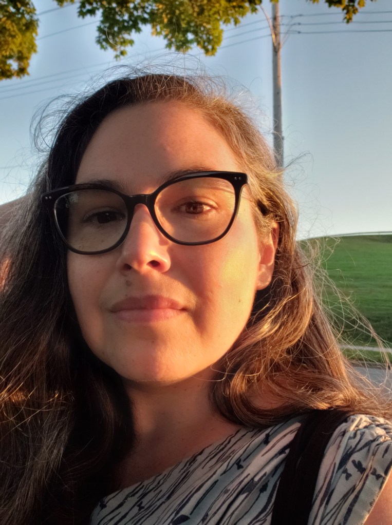 Andreae, a white woman with dark-rimmed glasses and salt-and-pepper hair, is looking at the camera with a slight smile. Her face and hair are washed in golden light.